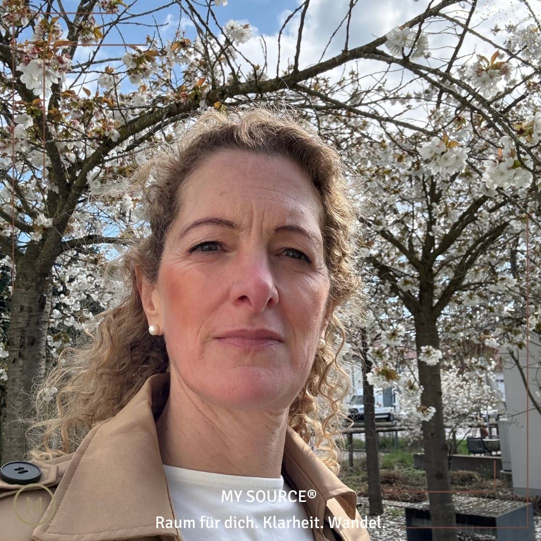 Frau unter blühenden Bäumen im Frühling, ruhig und präsent - Symbol für Wandel, innere Stabilität und natürliche Führung im Rhythmus der Zyklen